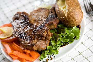 A juicy t-bone steak with baked potato and vegetables