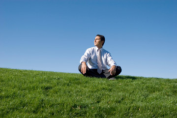 Businessman meditating on green grass