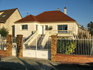Maison de banlieue blanche au toit rouge avec grille.