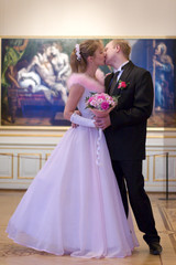 Fototapeta premium Bride and groom kissing indoors over picture background