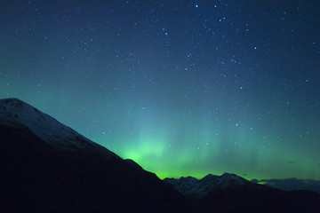 Northern lights making the sky green over the tops of mountains
