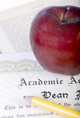 A red apple and pencil lay on top of a diploma