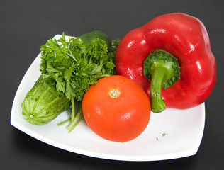 Fresh vegetables on a white plate and a black background