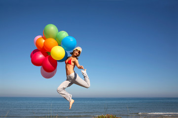 girl with colorful balloons jumping on the beach