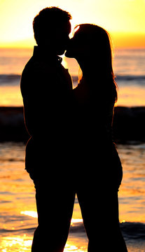 Silhouette of a young couple kissing on the beach at sunset