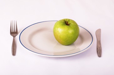 Green apple on with plate with fork and knife