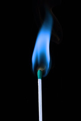 A single wooden match with a blue flame, over black.