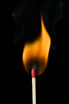 A single wooden match lit ablaze, over black.