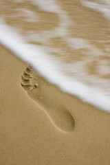 Footprint on the beach with little motion blurred wave