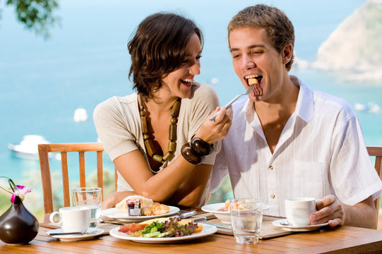A young couple enjoying breakfast outside with an ocean backdrop