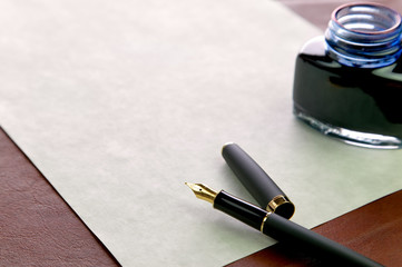 Fountain pen, expensive paper and inkwell on leather desktop