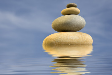 pile of zen round stones with blue sky and water reflexion