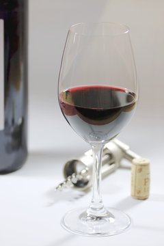 a glas of red wine and a wine bottle, the cork and the corkscrew