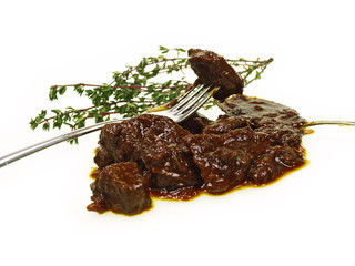 eine Portion Rindergulasch und ein Stück auf einer Gabel mit Thymian freigestellt auf weißem...