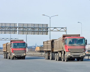 Red dump trucks ride in a line of my 