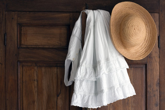 white cotton dress and straw hat on antique cabinet