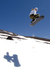 woman snowboarder in air after jump with shadow on snow