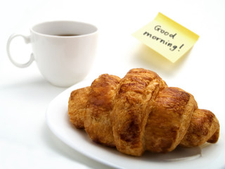 A croissant, a cup of coffee and a yellow note