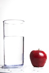 Apple next to a glass of water on white