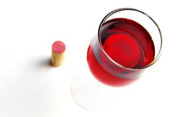 Glass of red wine and cork, on white