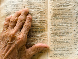 Wrinkled arthritic hand on opened old bible