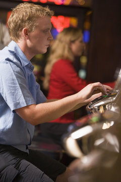 Man in casino playing slot machine with people in background