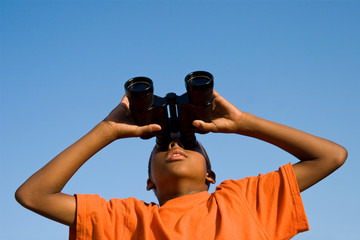boy with binoculars looks skyward at something to see