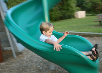 Fototapeta na wymiar young boy sliding on playground slide with motion blur