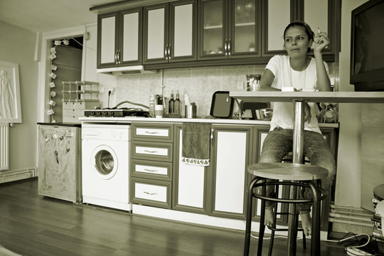 Young Woman Sitting At Kitchen Bar Table Smoking