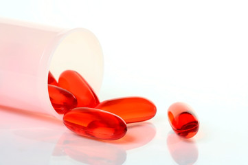 Translucent orange capsules with pill bottle on white background