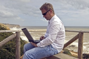 Young man working on his laptop at the beach
