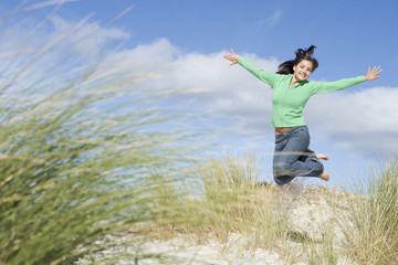 Fototapeta premium Young woman jumping amongst sand dunes