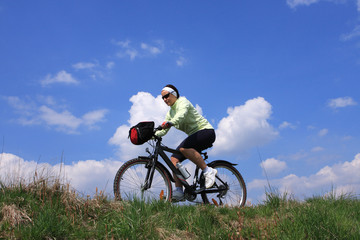 Fototapeta na wymiar Young lady cycling, blue sky background