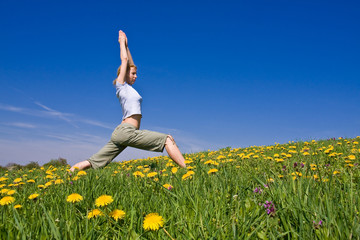 young female excercising yoga on flowery meadow