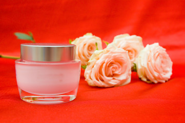 roses and cosmetic cream on a red background