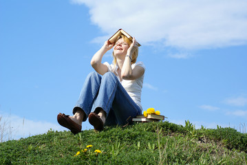 female student outdoor on gren grass with books and blue sky on