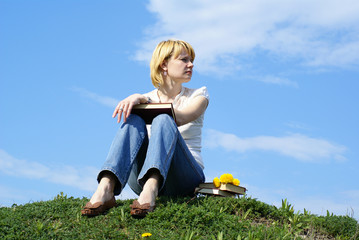 female student outdoor on gren grass with books and blue sky on