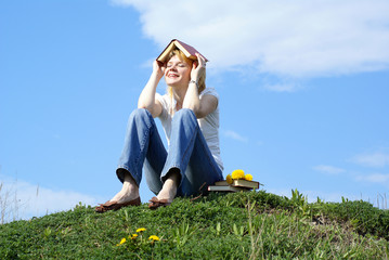 female student outdoor on green grass with books and blue sky on