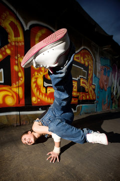 Girl break-dancer posing on a grunge graffiti wall