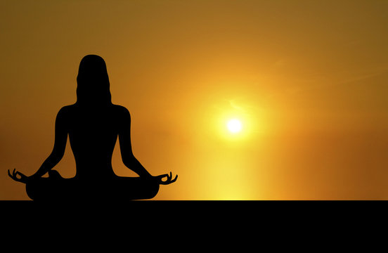 front silhouette of woman meditating on sunset background