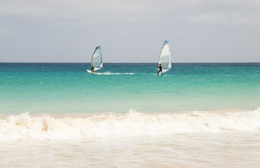 Two windsurfers racing across turquoise seas in Cape Verde.