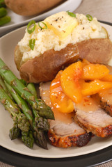 Sliced pork dinner with peaches, baked potato and asparagus