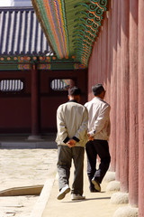 Two elderly men walk along an outdoor corridor.