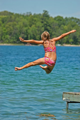 Young Girl Jumps Off Dock into Lake Extending Arms and One Leg