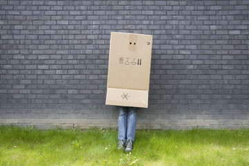 boy standing against a wall with a cardboard box over his head