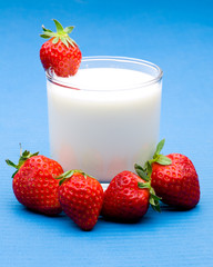 Mehrere Erdbeeren um ein Glas mit Milch