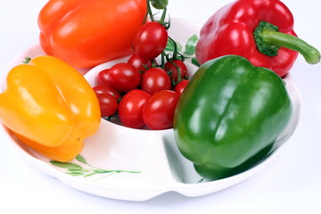 Four colorful peppers and small tomatoes on white plate
