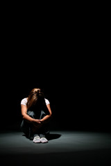 Woman sitting in a spotlight with her head on her knees.