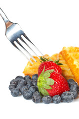 Waffles, blueberries and the fork pricking the strawberry