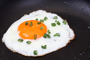 A close up for a egg with chive in a frying pan